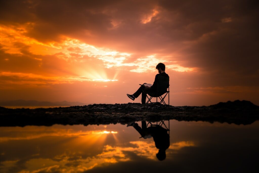 Man reading book while sitting on lake shore and contemplating life.